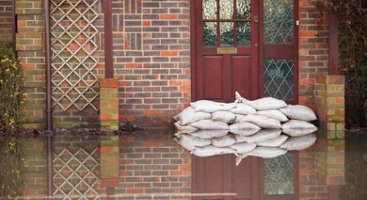 Sandbags stacked in front of a red door to protect a brick house from rising floodwaters.